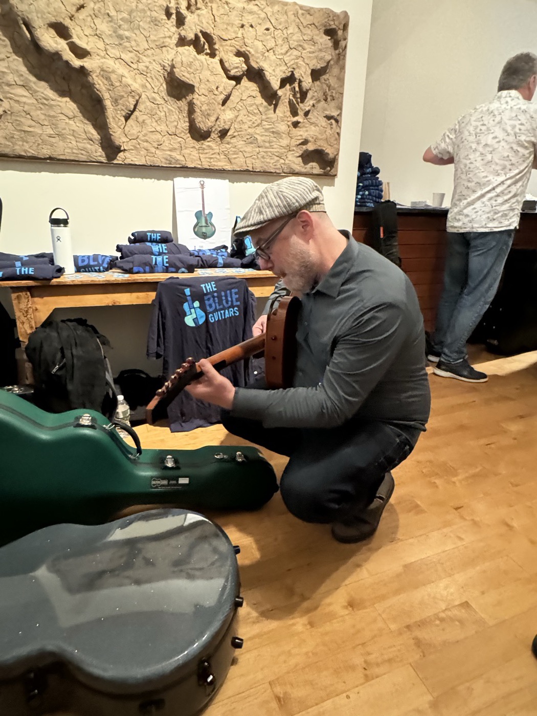 A player kneeling near a green guitar case while trying an instrument.