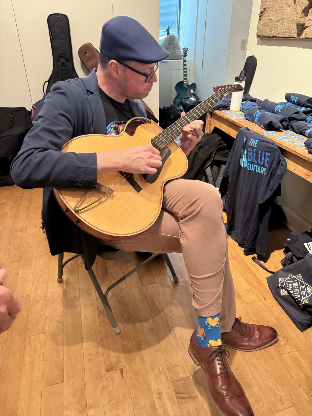 A seated guitarist playing a nylon-string instrument near Blue Guitars materials.