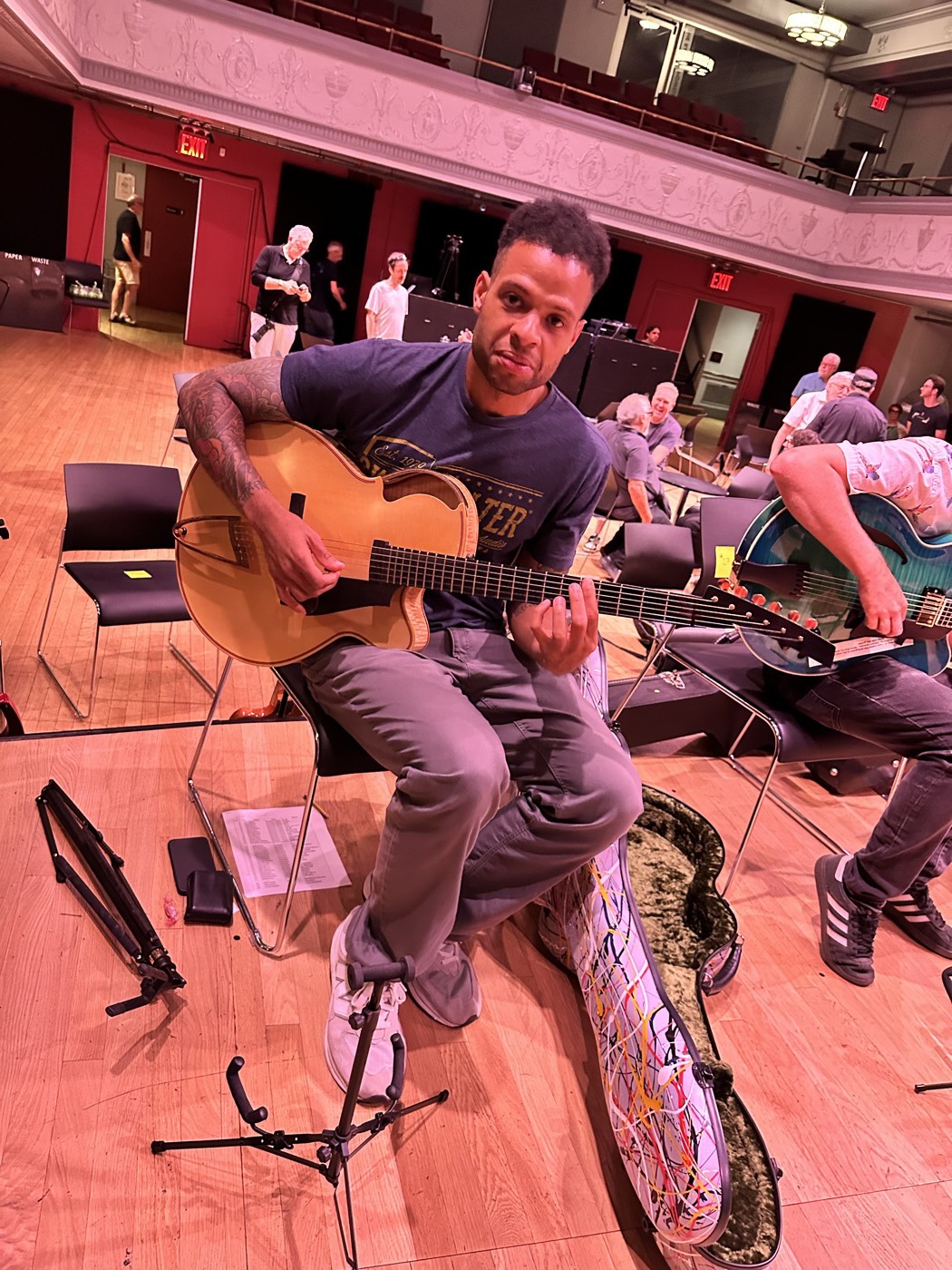 A guitarist testing an archtop on a stage-like floor with cases nearby.