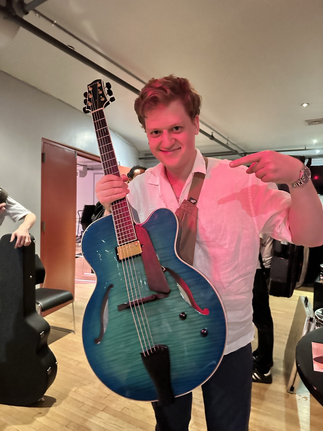 A player holding a blue archtop guitar in the previous event room.