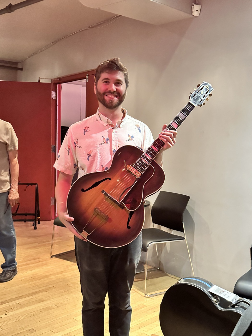 An attendee smiling while holding a deep archtop guitar.