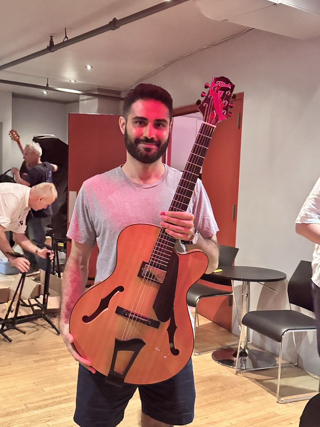 An attendee holding a natural-finish archtop guitar in the event room.