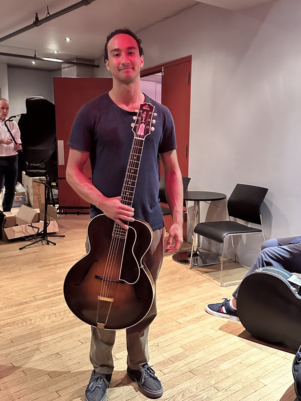 An attendee standing with a dark sunburst archtop guitar.