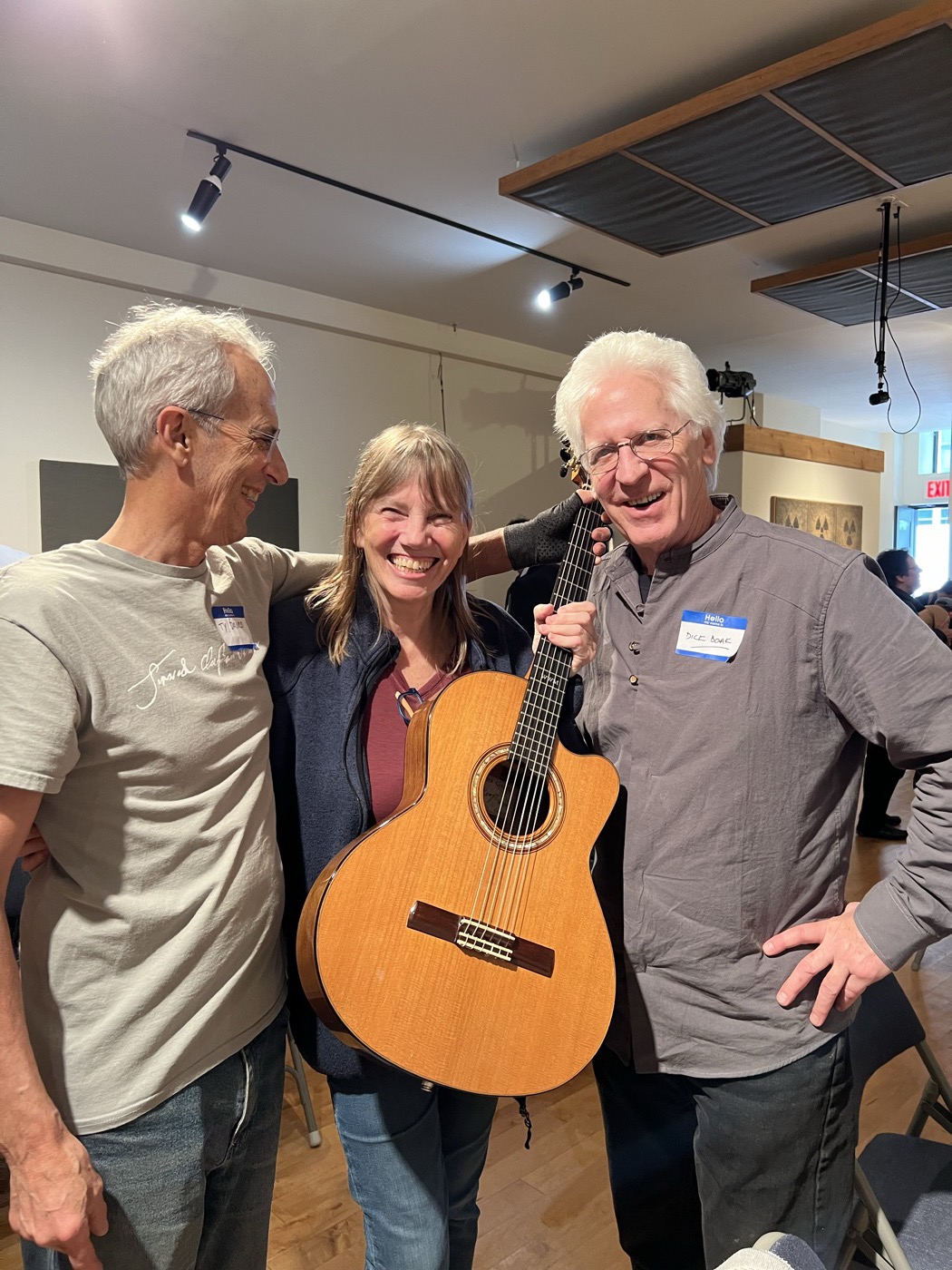 Three attendees standing together with an acoustic guitar in the previous event room.