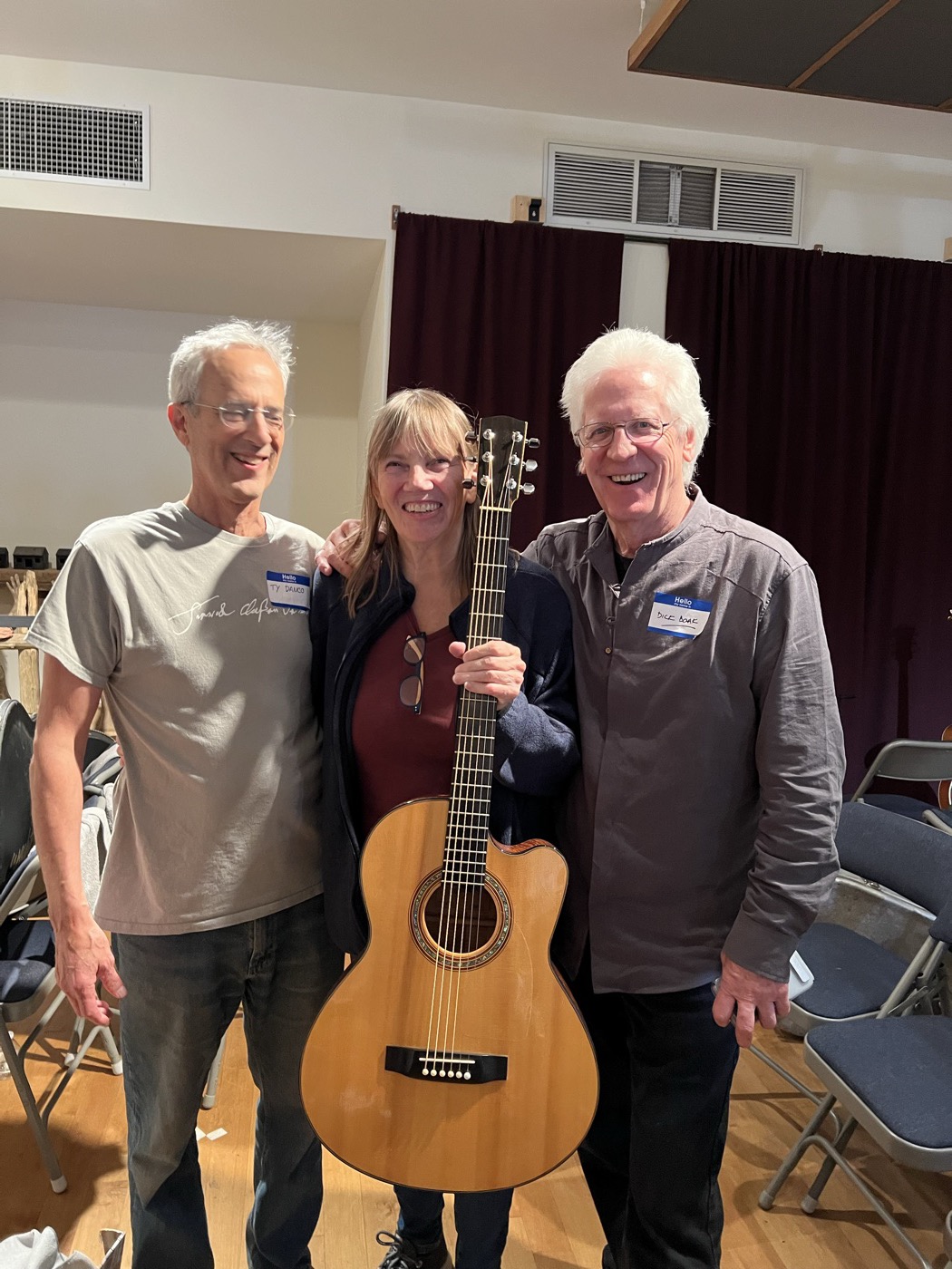 Three attendees smiling together with a guitar in the previous event room.